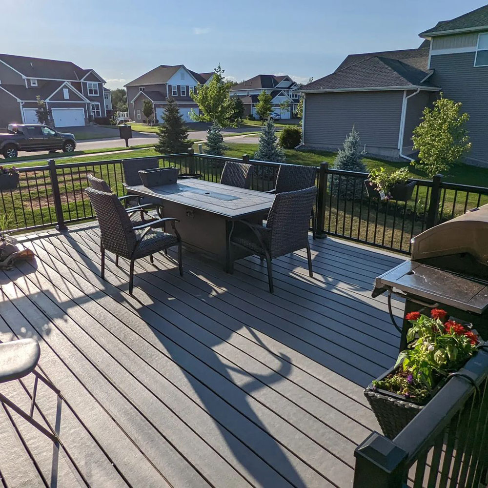 An open deck with aluminum railings, a rectangular table with six modern rattan chairs and plant ornaments hung on the railings