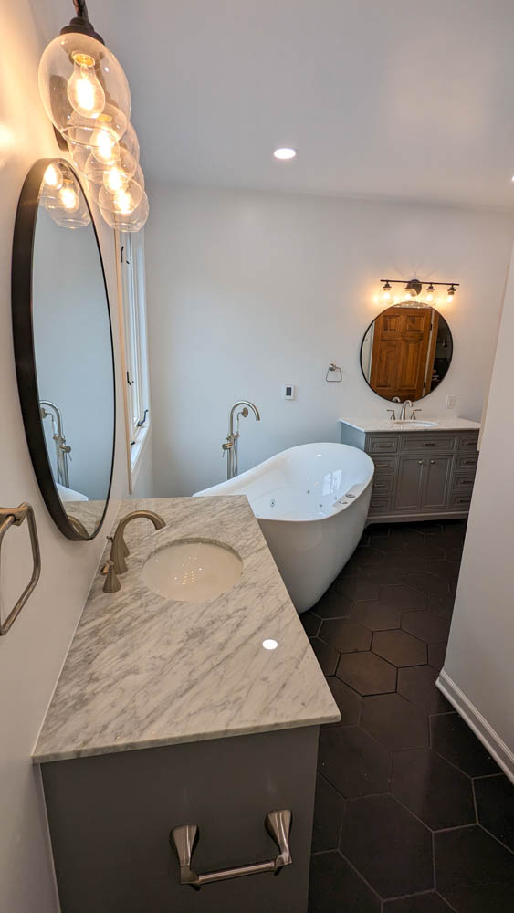 Freestanding Tub in a bathroom with free standing faucet, a casement type window, warm light fixtures, and vanity cabinets for bathroom storage