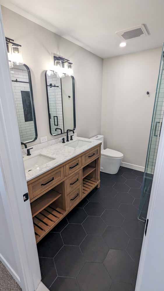 Bathroom; view from the outside, a vanity cabinet with two sink and two mirrors with wall mounted pendant lights, large dark blue hexagonal flooring tiles