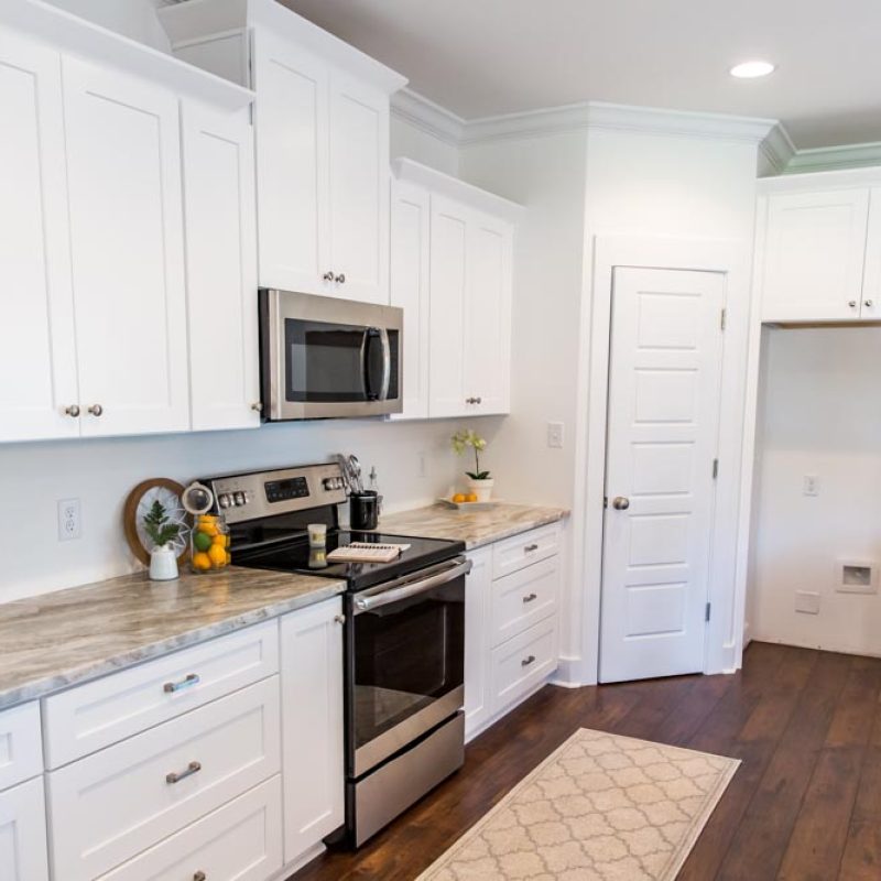 Newly constructed modern kitchen with white cabinets, marble countertops and hardwood floor